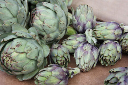 a pile of fresh artichokes sitting on a fiber board table